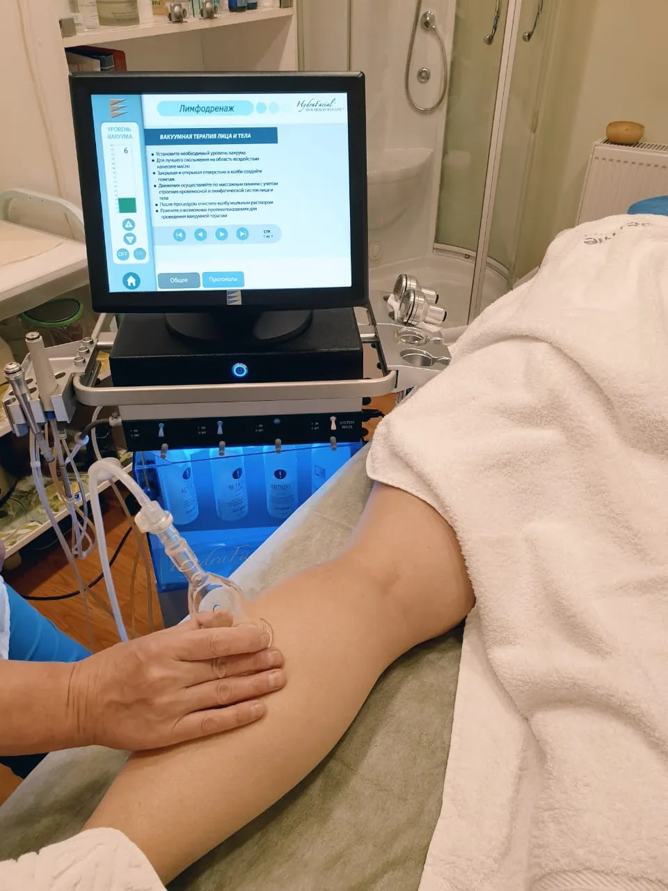Специалист проводит процедуру вакуумного лимфодренажа, рядом аппарат с экраном